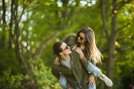 Man giving his pretty girlfriend a piggy back in the park smiling at camera on a sunny dayの写真素材
