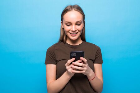 Front portrait of young smiling woman using mobile phone against blue background
