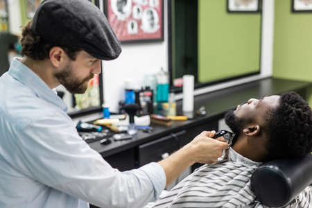 Barber is going through the electric cutting and shaving machine for the beard of an African-American boy.の写真素材