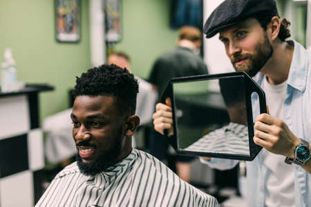 Closeup of process of trimming of hair in barber shop. Qualified barber keeping clipper in hands and correcting shape of hair to male client sitting on chair.の写真素材