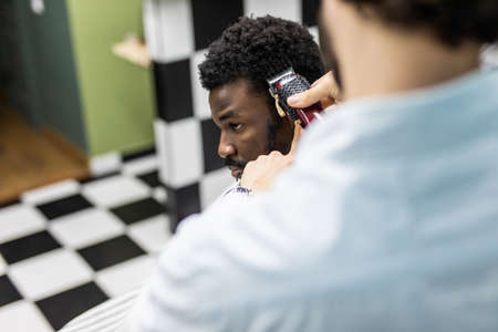 Closeup of process of trimming of hair in barber shop. Qualified barber keeping clipper in hands and...