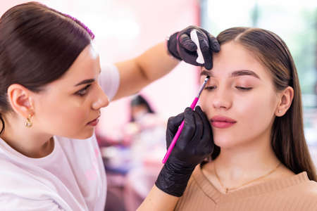 Beautiful young woman gets eyebrow correction procedure. Young woman painting her eyebrows in beauty saloon.の写真素材