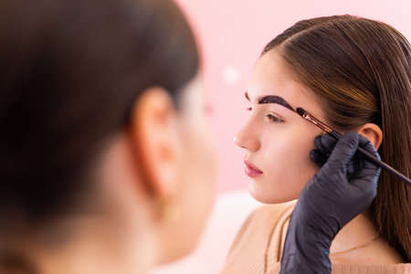 beautician- makeup artist applies paint henna on previously plucked, design, trimmed eyebrows in a...