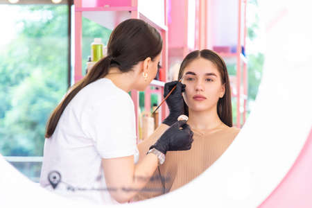 Beauty master brow painter paints eyebrows by coloring them with henna. Woman makes a make-up working in black gloves in a beauty salon. Concept brow architectureの写真素材