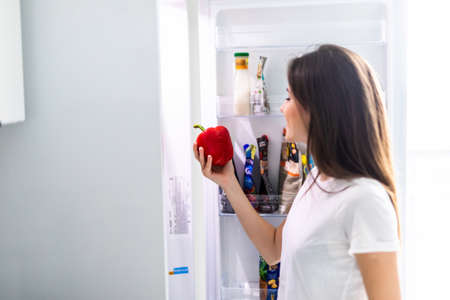 Diet. Beautiful young woman near the fridge with healthy food. Fruits and vegetables in the refrigerator. Vegan foodの写真素材
