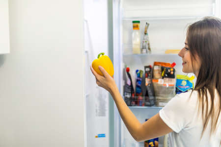 Beautiful Young Woman near the Refrigerator with healthy food. Fruits and Vegetables in a Fridgeの写真素材