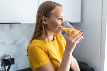 Attractive woman holding a glass of orange juice while standing in the kitchen