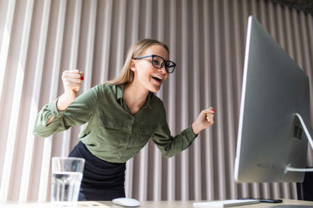 Excited executive wearing suit raising arms watching a desktop monitor at officeの写真素材