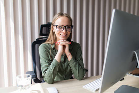 Portrait of businesswoman sitting at bright modern work station and typing on pc