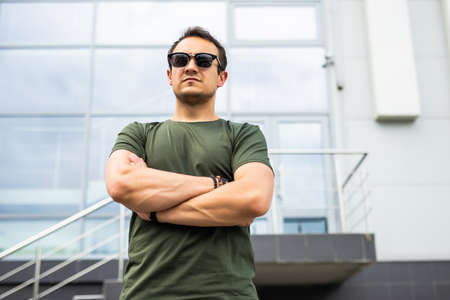 Handsome smiling young man with folded arms. Beautiful portrait of laughing joyful cheerful men with crossed hands in a cityの写真素材