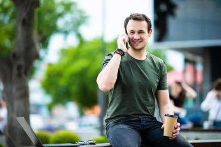 Portrait of handsome businessman with cup of coffee talking by phone outdoorsの写真素材
