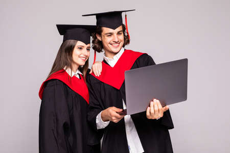 Young graduation couple holding laptop isolated on white backgroundの写真素材