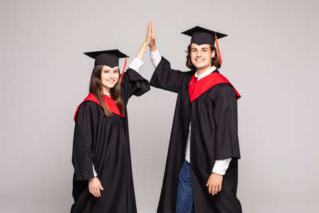 Two happy college graduates giving high five smiling after receiving diplomas on white background.の写真素材