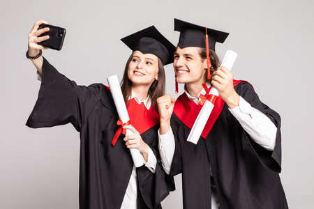 Male and female student taking a selfie with mobile phone isolated on white backgroundの写真素材
