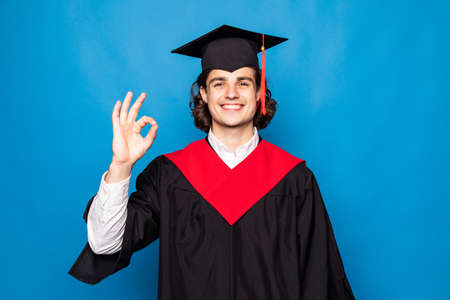 A happy graduate with a thumbs up sign, isolated on blueの写真素材