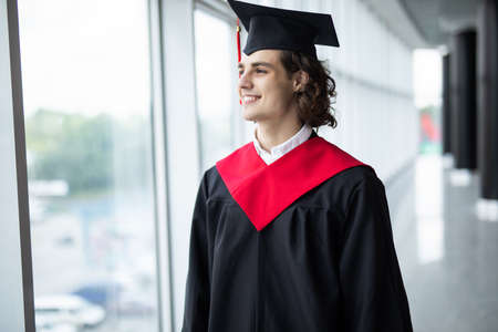 happy young man in graduation cap smiling and gesturing in universityの写真素材