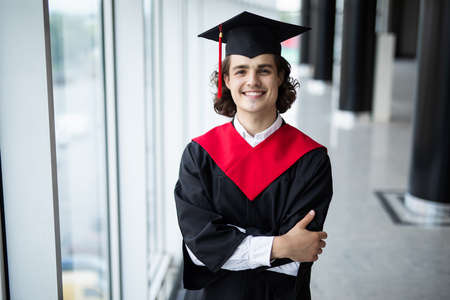 happy young man in graduation cap smiling and gesturing in universityの写真素材