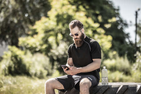 Handsome young sportsman with phone resting after cross training exercises. Healthy lifestyle concept. Drink waterの写真素材