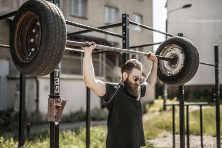 Athletic man working out with a dumbbell from tires. Strength and motivation. Outdoor workout....