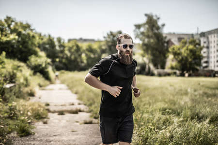 Young happy cheerful smiling bearded man, during morning jogging outdoors.の写真素材