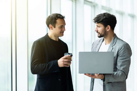 Two cheerful businessmen discussing something on the laptop and smiling in an officeの写真素材