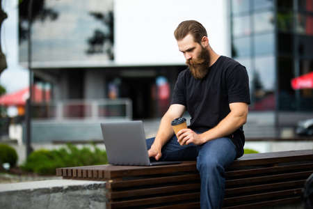 Young handsome man sitting on the park bench using laptop outdoorsの写真素材