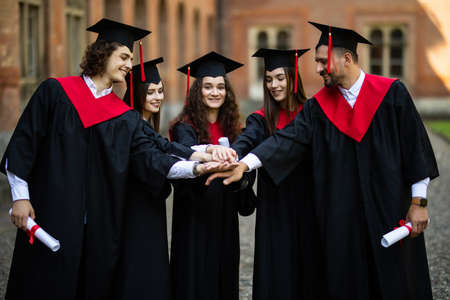 education, graduation and people concept - group of happy international students in mortar boards and bachelor gowns making high fiveの写真素材
