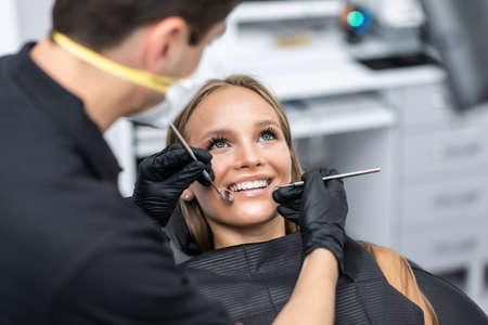 Dentist examining patient teeth with a mouth mirror and dental excavator.