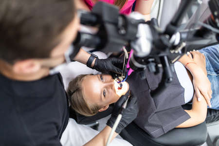 Dentist is treating female patient's teeth at stomatolory office with microscope.