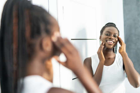 African woman after shower wrapped in towel looking in mirror found facial wrinkles facial lines...