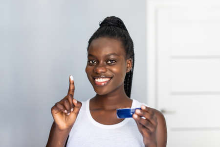 Keeping her skin fresh and smooth. Beautiful young African woman spreading cream on her face and smiling while standing against a mirror in bathroomの写真素材