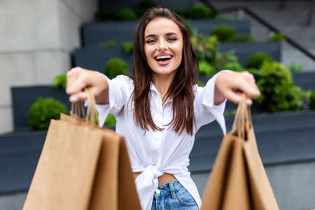 Happy shopper wearing red coat showing shopping bags and pointing you in the streetの写真素材