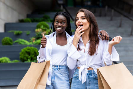 sale, consumerism and people concept - happy young women looking into shopping bags at shop window in cityの写真素材