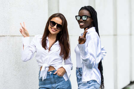 Two young beautiful smiling girls in trendy summer dresses having fun in sunglasses shows peace signの写真素材