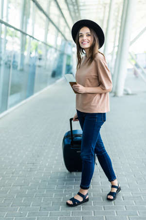 Full length side portrait of a happy business woman walking with suitcase and talking on mobile phone at airportの写真素材