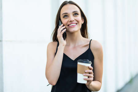 Girl with coffee cup talking on the phone and walking at the city street
