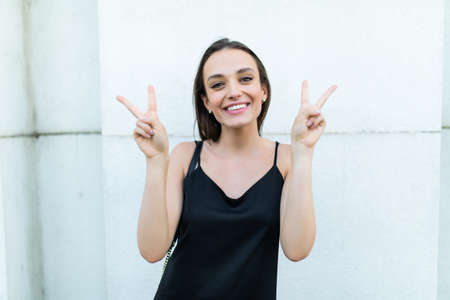 Happy brunette woman taking selfie photo and gesturing peace sign in street cafe outdoorsの写真素材