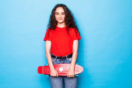 Portrait of woman posing with skateboard on blue background