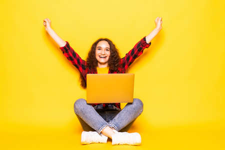 Young woman sitting using laptop and celebrating victory and success over yellow backgroundの写真素材