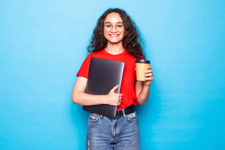 Young woman looking side holding laptop drinking coffee on blue background