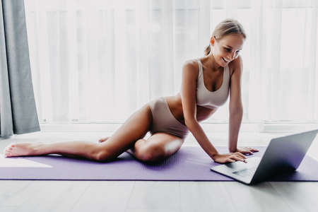 Sporty woman in sportswear working out and using laptop at home in living room.の写真素材