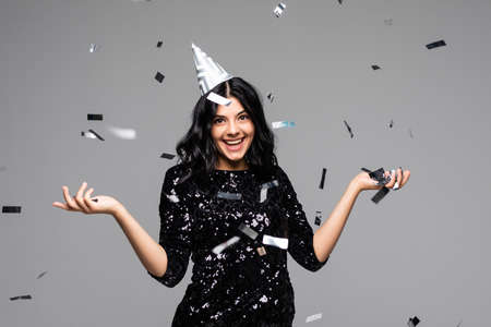 Beautiful woman celebrating Birthday while confetti falling on her on gray backgroundの写真素材