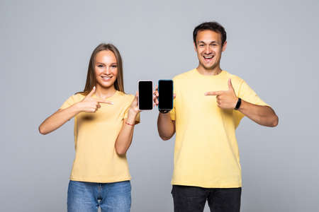 Portrait of a smiling couple standing and holding mobile phones pointed on screen isolated on the...