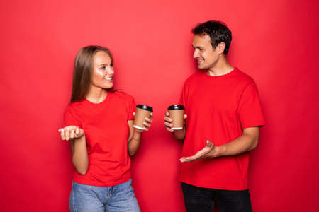 Young couple holding coffee paper cups isolated over red background