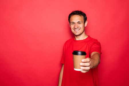 Young handsome man drinking a cup of hot coffee over red isolated backgroundの写真素材