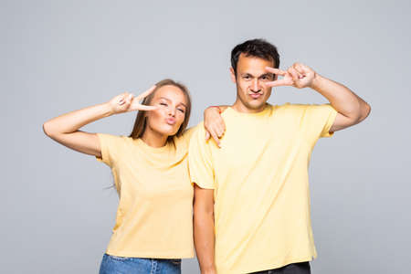Lovely couple showing peace symbol near their eyes, standing isolated over gray backgroundの写真素材