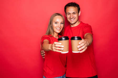Young couple holding coffee paper cups isolated over red backgroundの写真素材