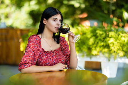 Photo of beautiful young woman sitting in cafe outdors in park with book holding glass drinking wine.の写真素材