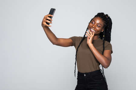 Portrait of a smiling afro american woman making selfie photo on smartphone over gray backgroundの写真素材