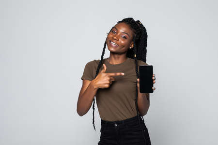 Portrait of woman showing black touch screen of smart phone pointing isolated on gray backgroundの写真素材